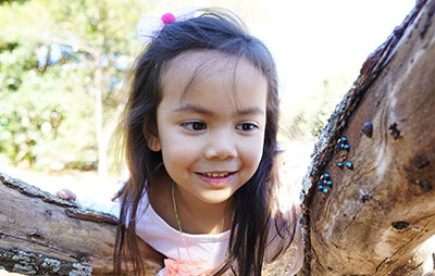 Girl poking head through tree during Nature Play