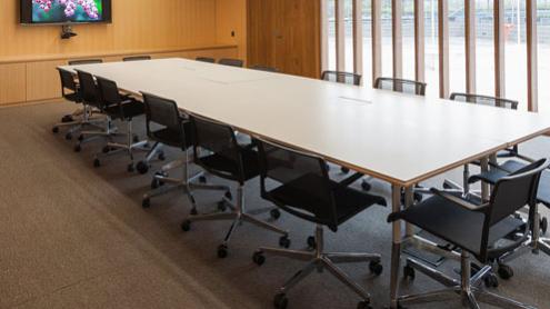 Corporate meeting room with wood panelling, wall to ceiling windows, a large meeting table with seating and a presentation screen.